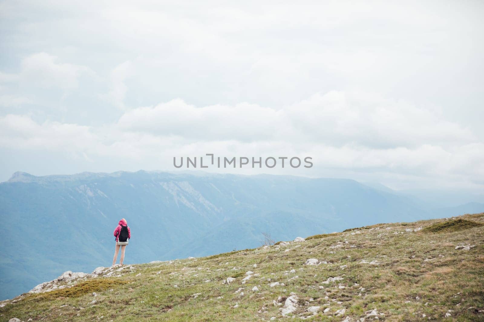 a woman on a hike stands on a mountain and looks at the mountains nature hiking journey by Simakov