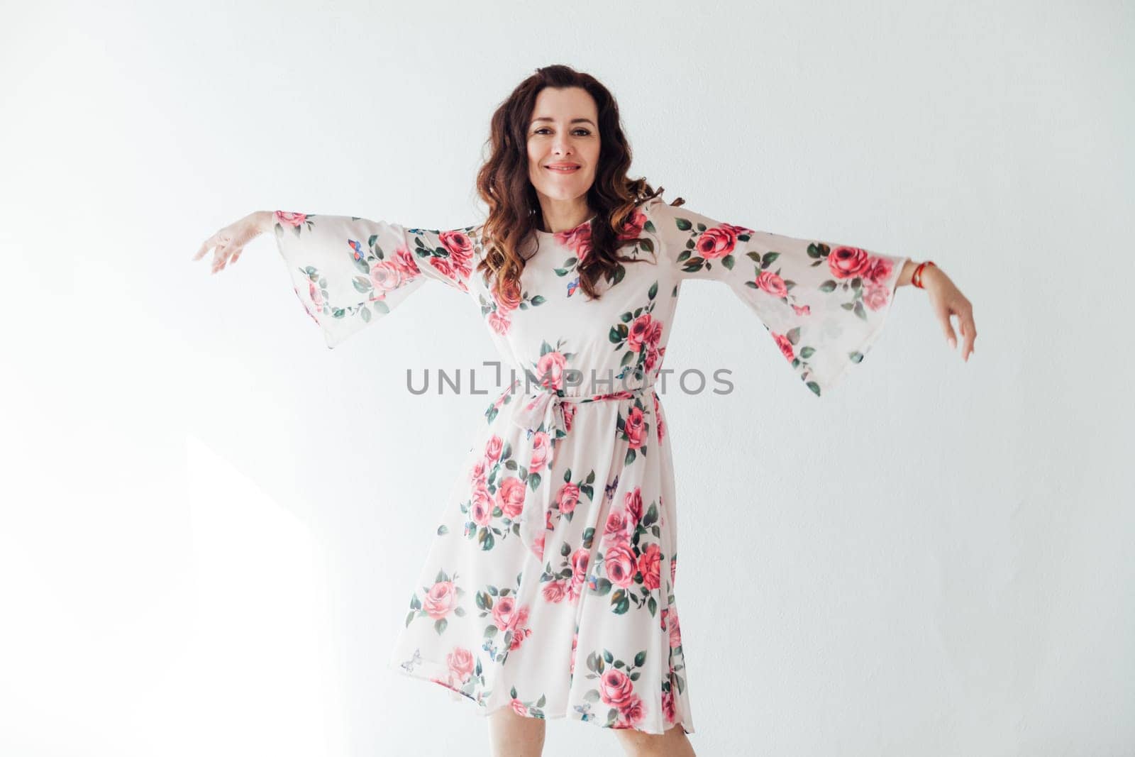 a woman in floral dress stands against a white wall on a white background