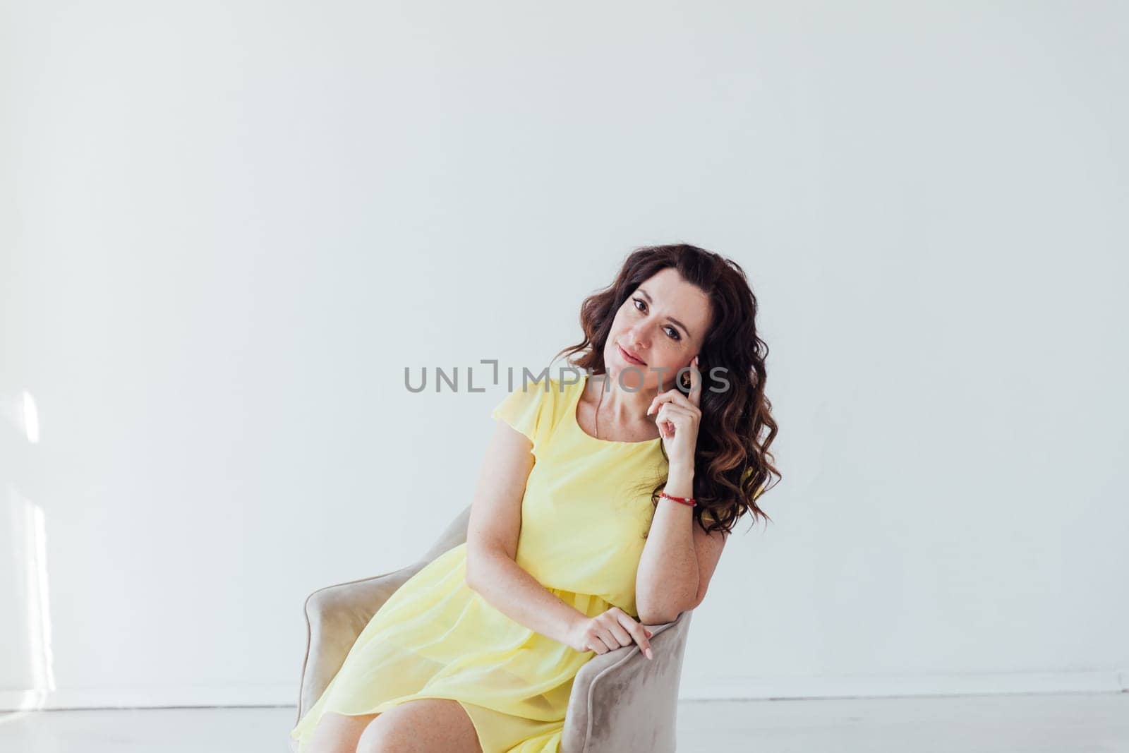 brunette woman in a yellow dress sits in a chair in a bright room