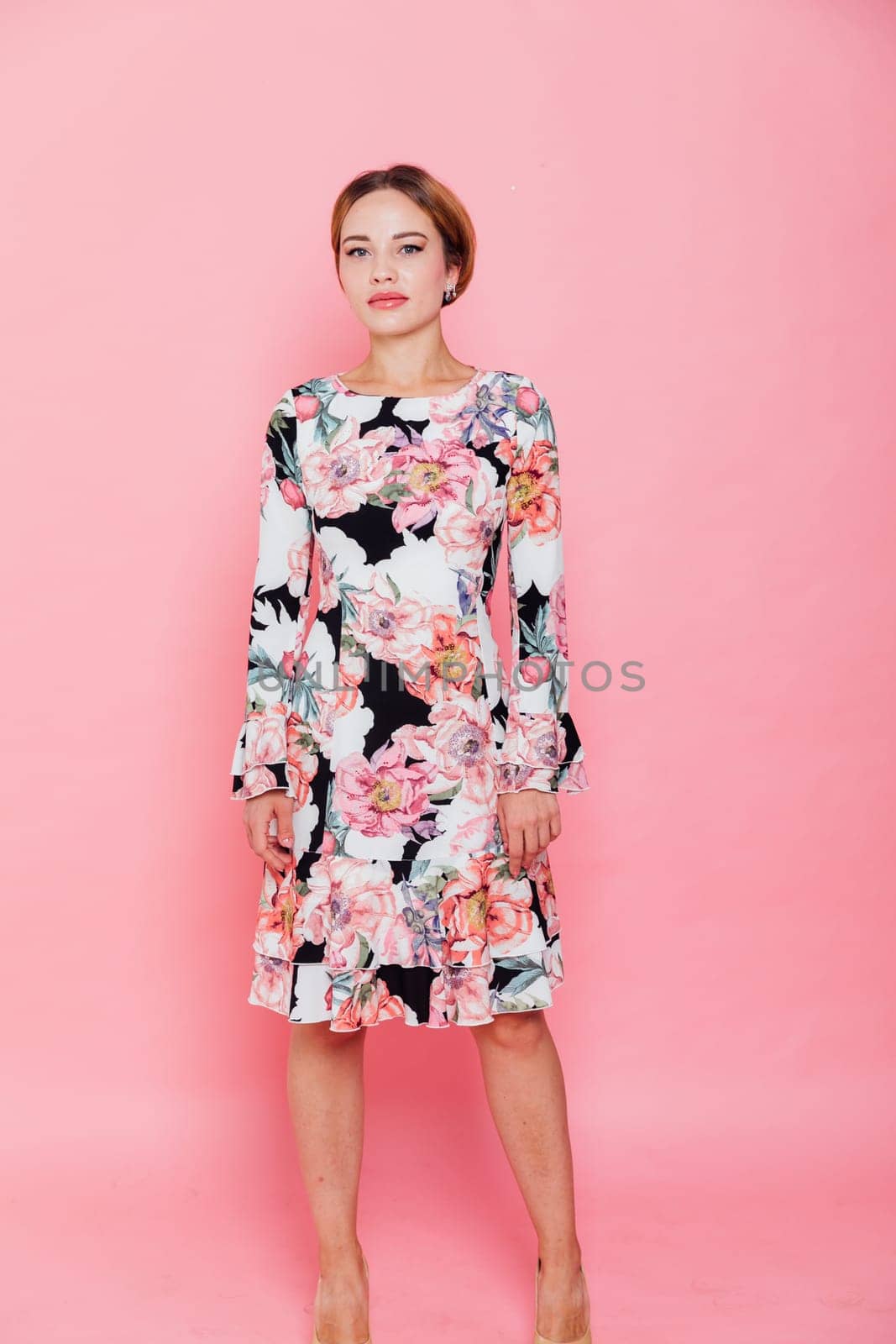 woman in a floral dress stands against a pink wall