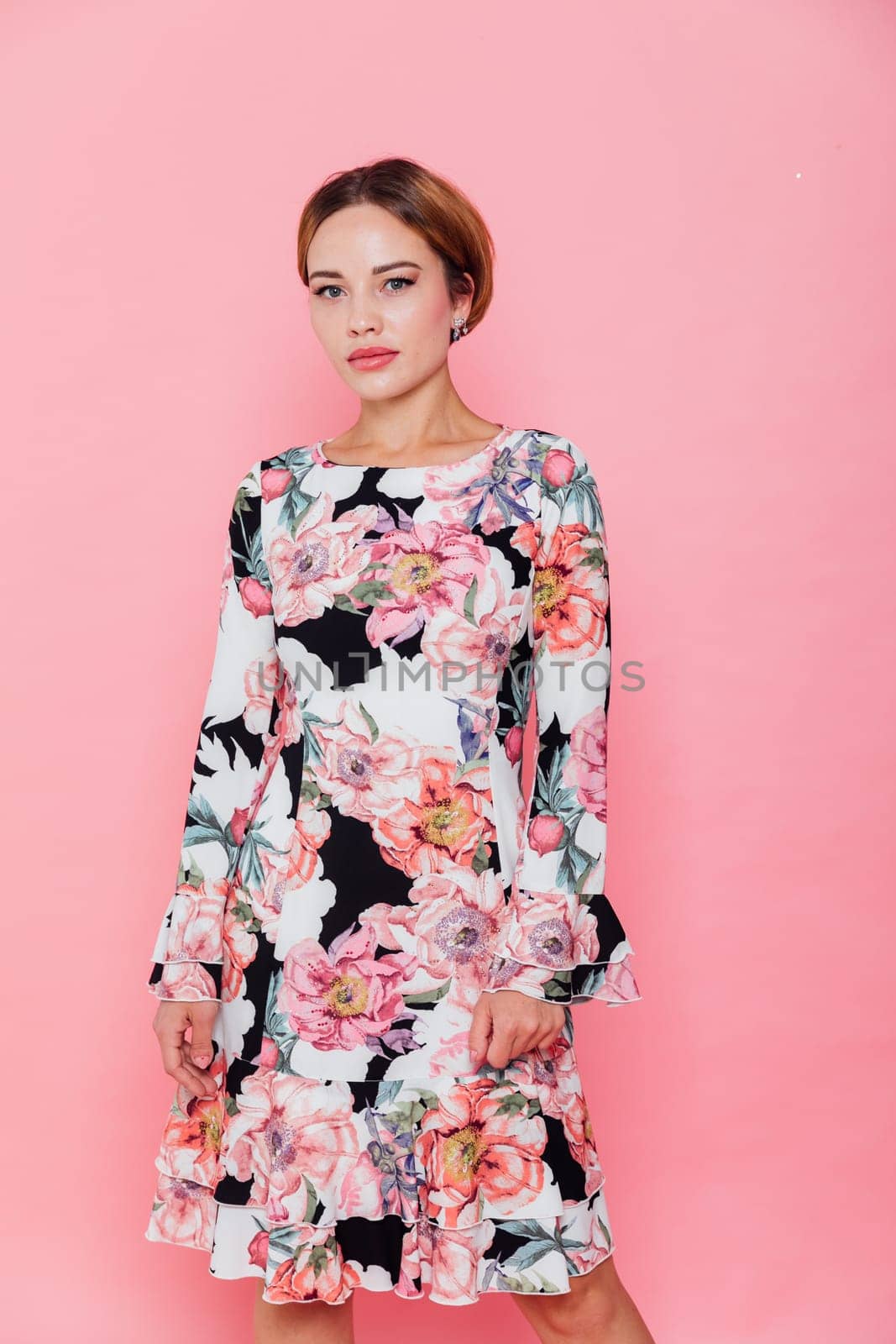 woman in a floral dress stands against a pink wall