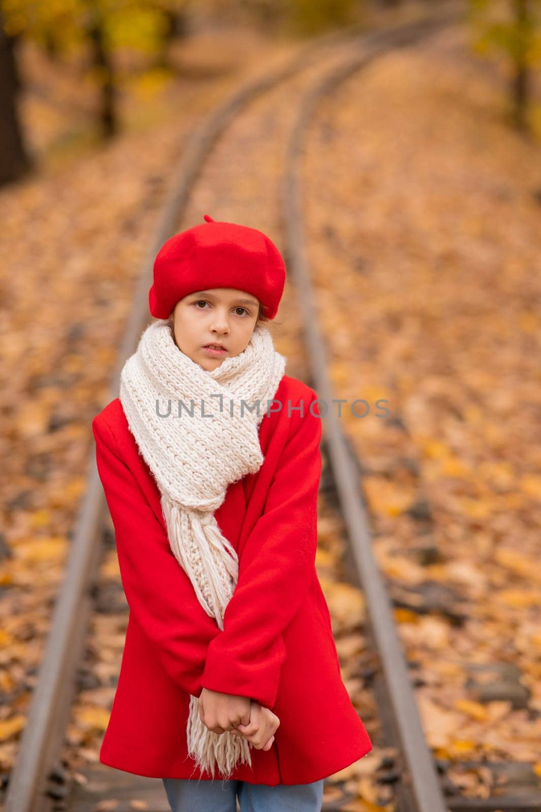 Caucasian girl in a red coat and beret walks along the railway tracks in the park in autumn