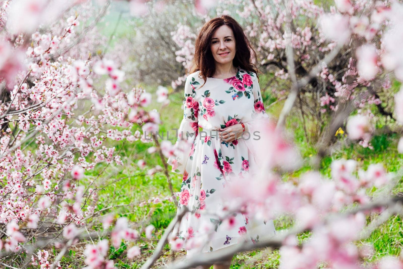 brunette in beautiful dress in pink flowers in a blooming garden walk in spring