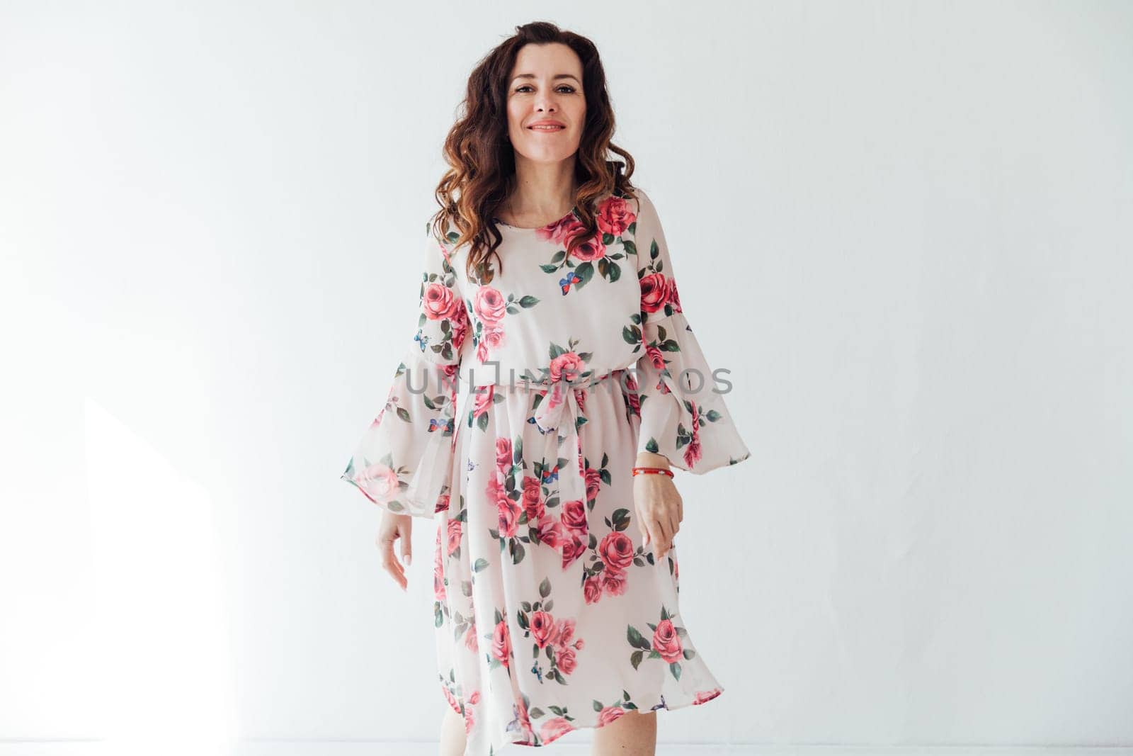 brunette woman in a floral dress poses on a light background in a room
