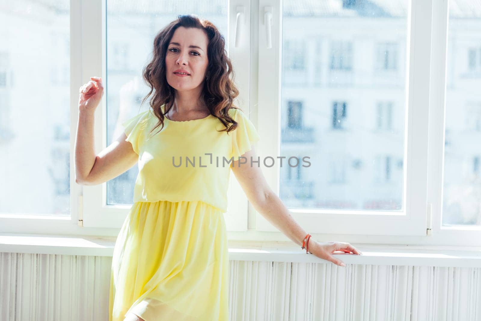 brunette woman standing by a window in a bright room