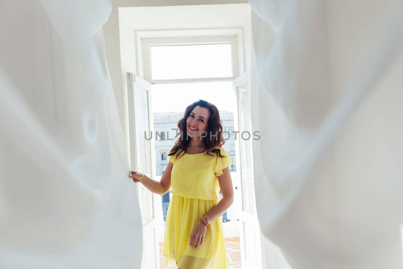 woman in a yellow dress stands at the balcony door of a bright room