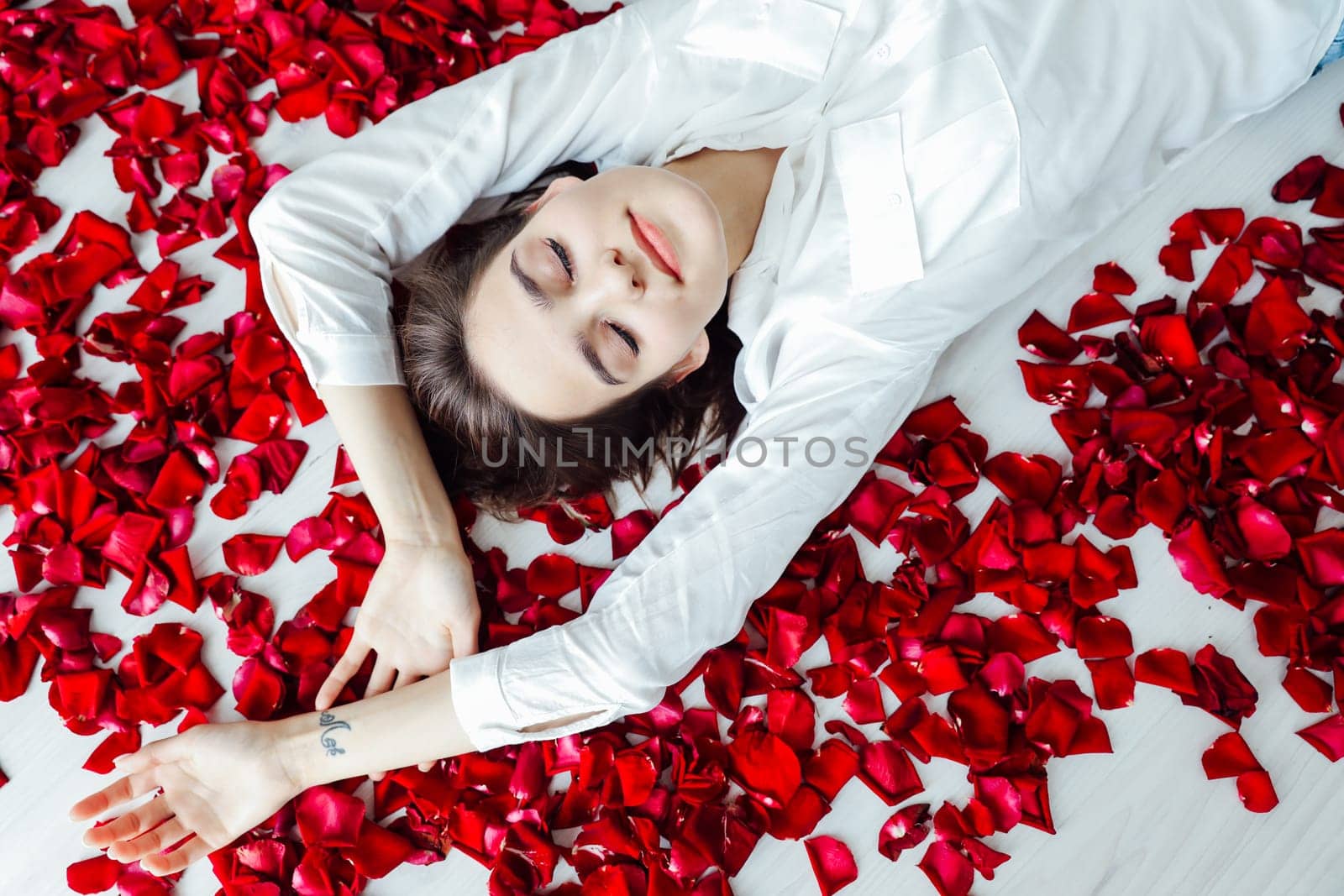 a woman lies on the floor with her eyes closed in red rose petals