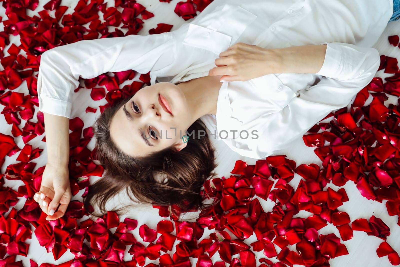 a woman lies on the floor in red rose petals by Simakov