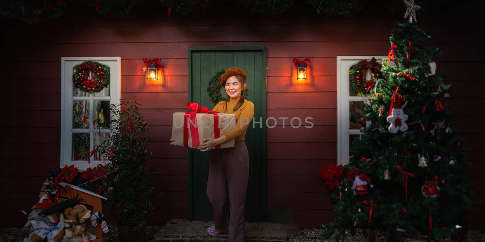 Happy woman wearing Santa hat holding of gift box. Positive emotional Santa girl. with a beautifully decorated Christmas tree serving as the background. festive Xmas concept.