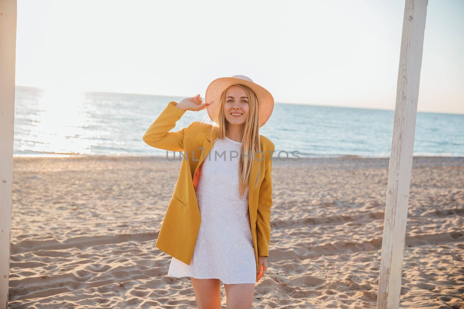a beautiful blonde in a hat stands on the sand by the sea