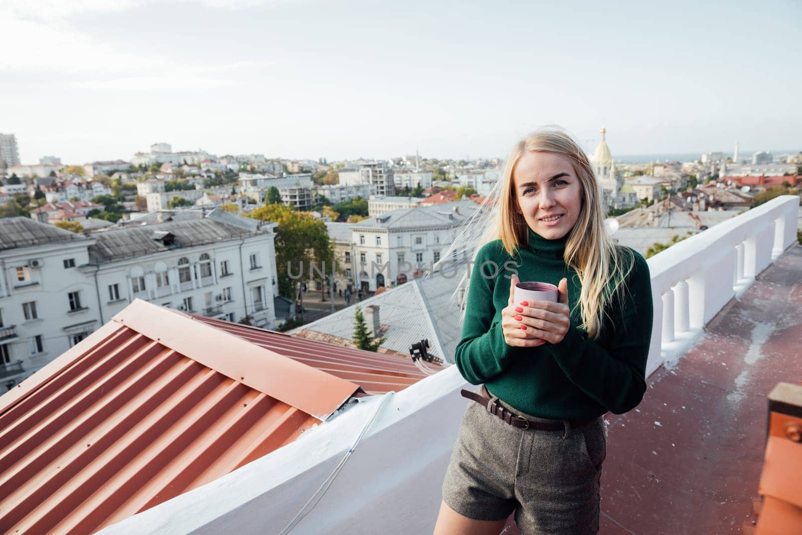 blonde beautiful woman with a mug on the roof of a house on the street