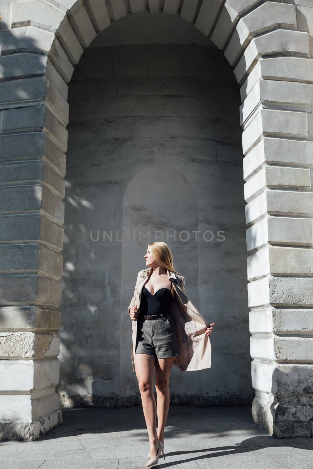 blonde fashionable woman in a raincoat stands against the wall outside walk rest