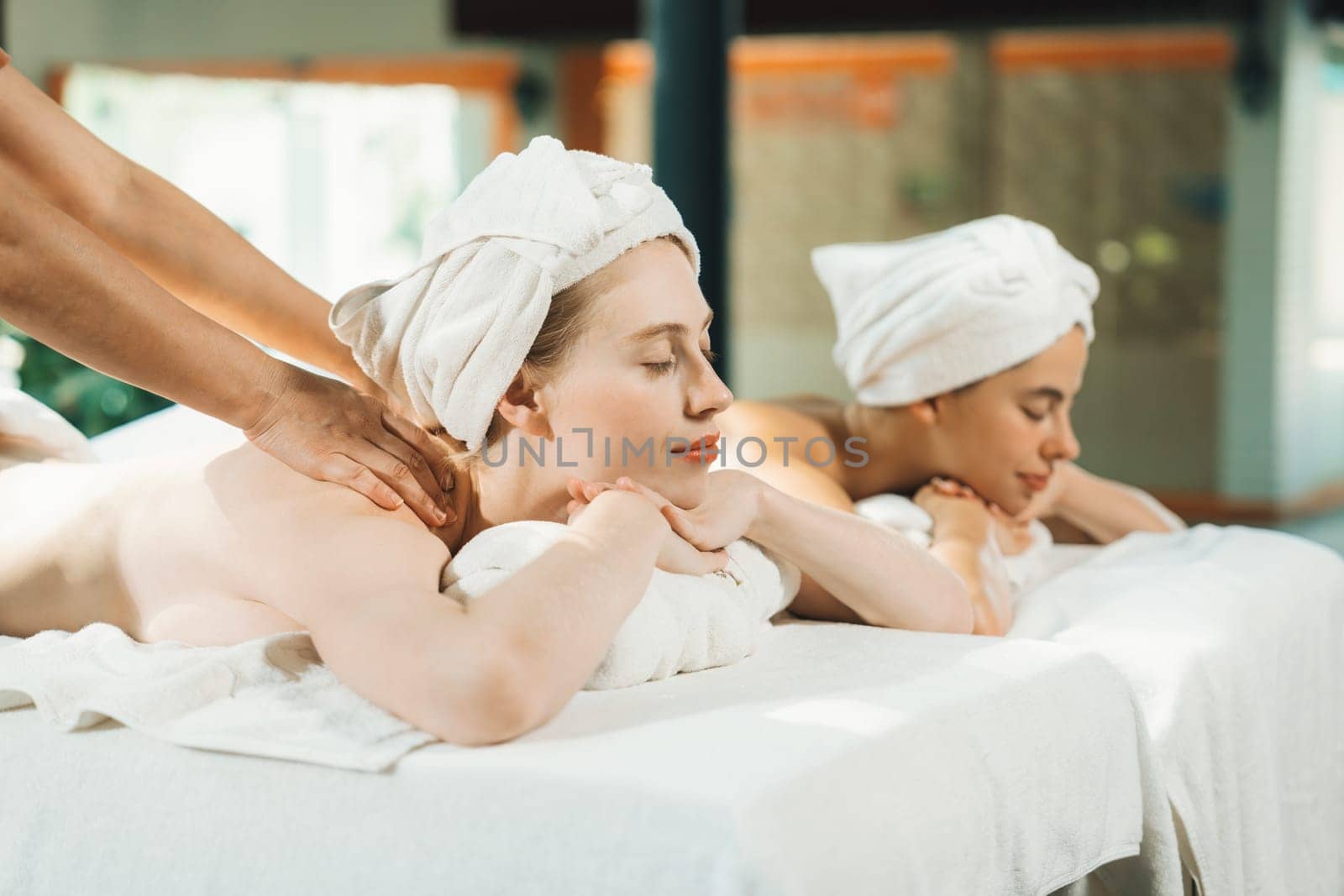 Couple of beautiful young woman lie on white spa bed during having back massage. Attractive caucasian woman having back massage at traditional spa room. Relaxing and healthy concept Tranquility.