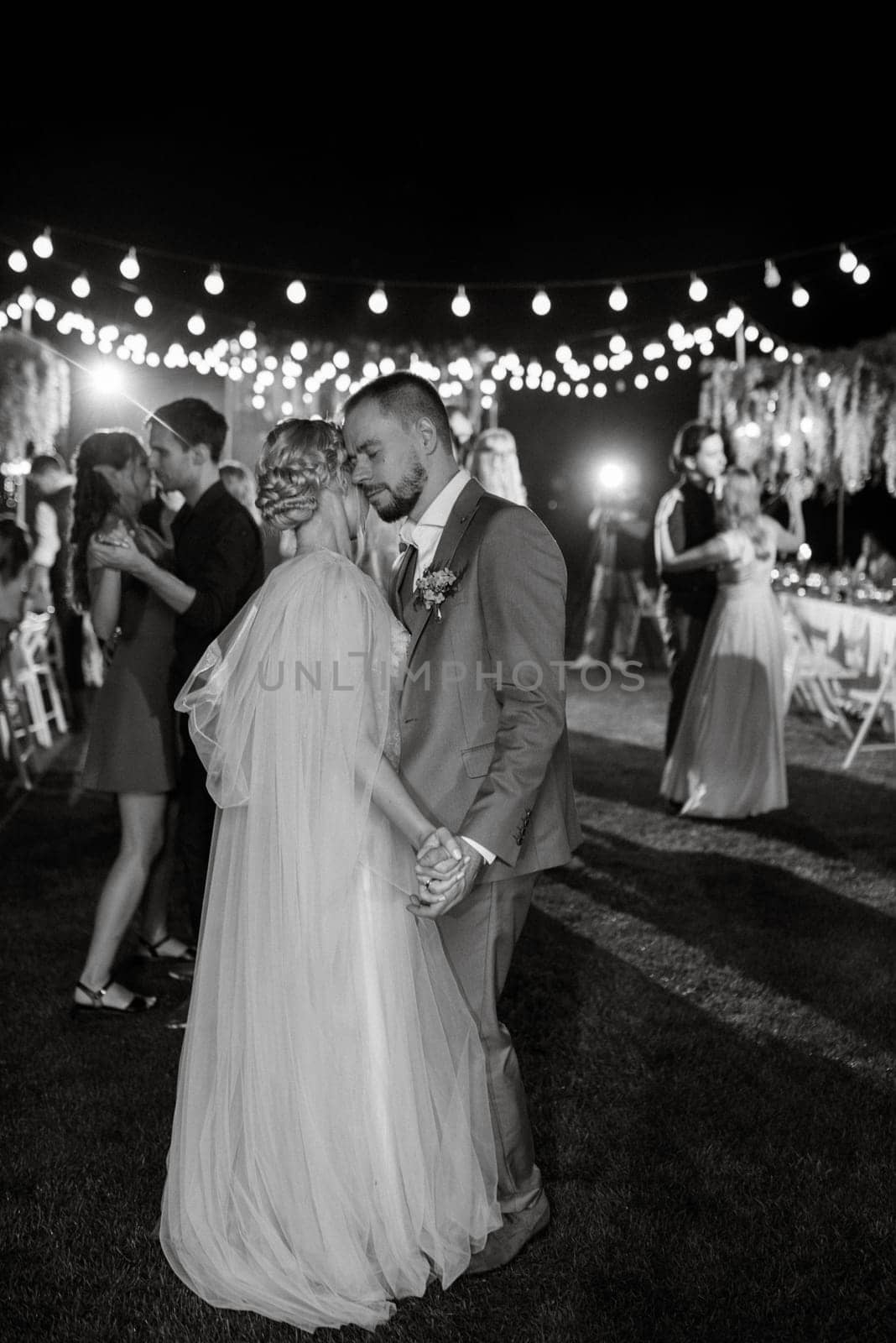 the first wedding dance of the bride and groom in the glade of the country club in the light of sunset and warm garlands