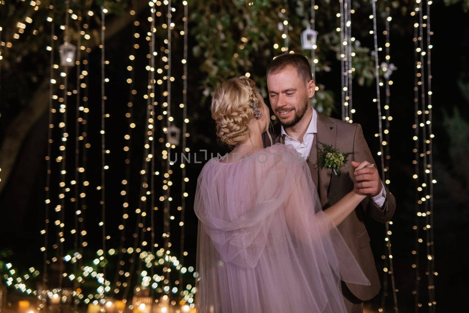 the first wedding dance of the bride and groom in the glade of the country club in the light of sunset and warm garlands