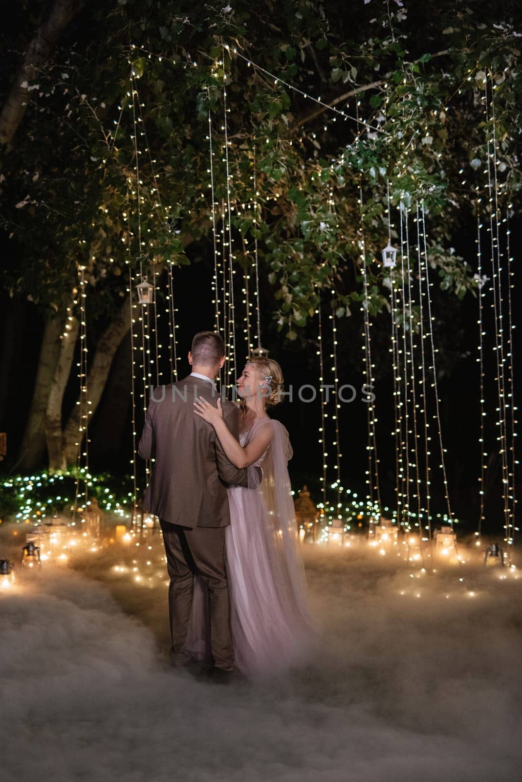 the first wedding dance of the bride and groom in the glade of the country club in the light of sunset and warm garlands