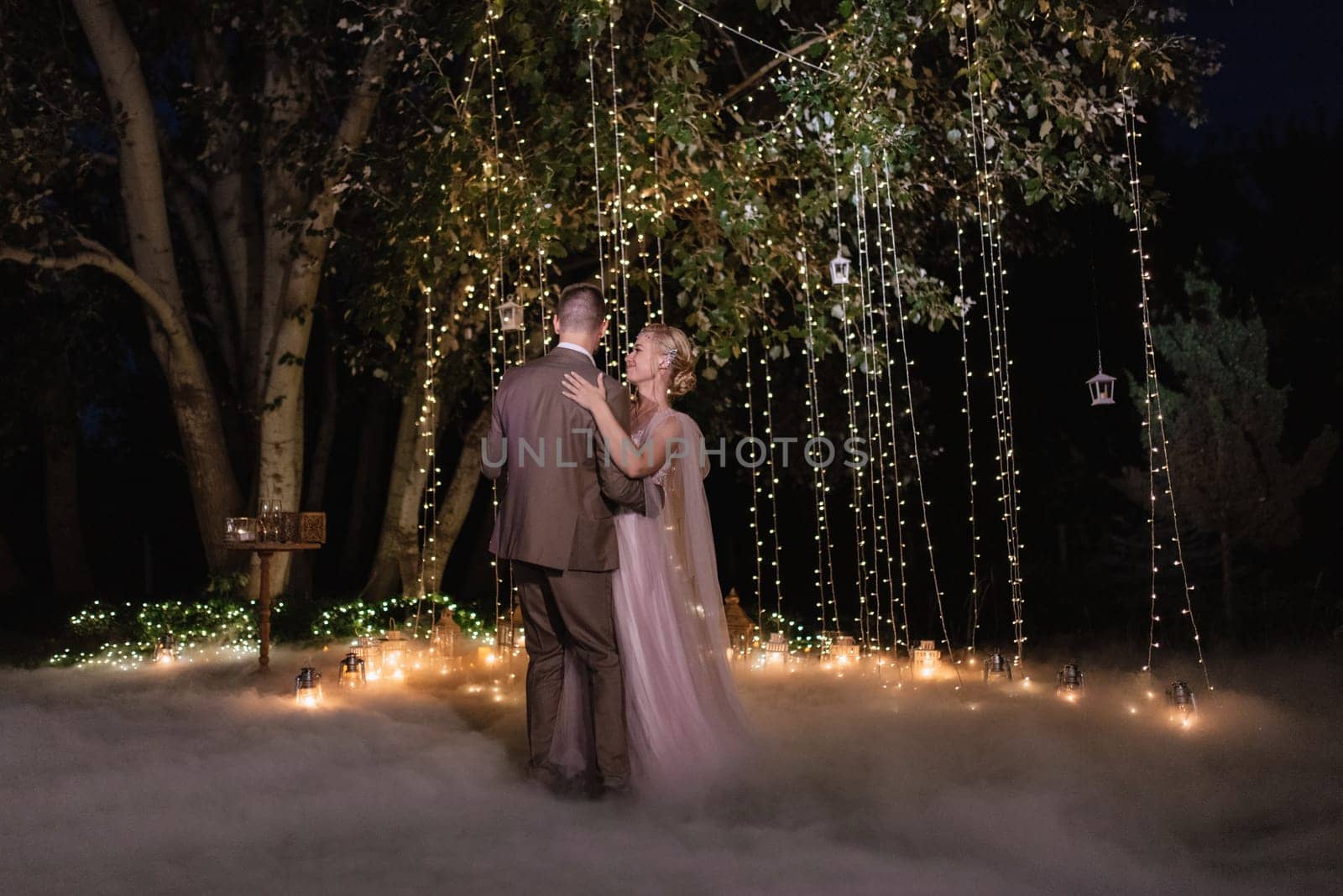 the first wedding dance of the bride and groom in the glade of the country club in the light of sunset and warm garlands