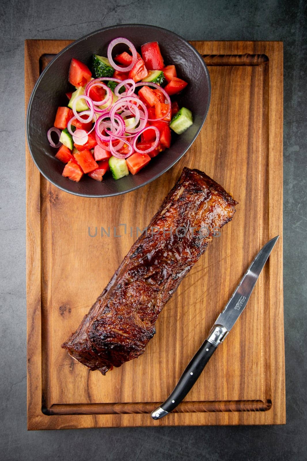 well-done steak with tomato and cucumber salad on a wooden tray