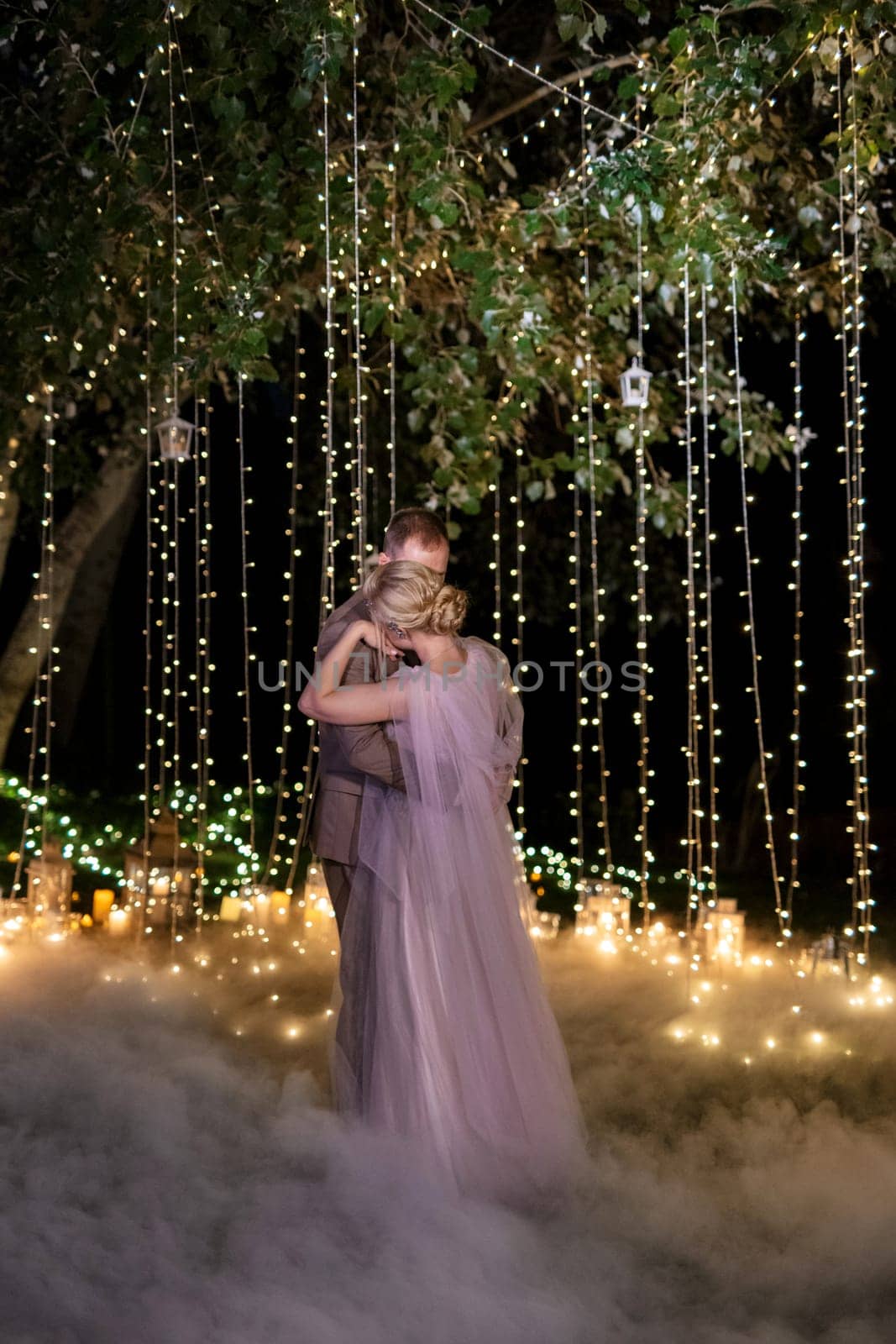 the first wedding dance of the bride and groom in the glade of the country club in the light of sunset and warm garlands