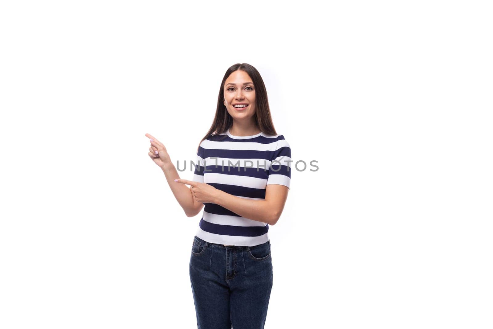 attractive young caucasian brunette woman in a striped t-shirt points with her hands to the advertising space on a white background with copy space.