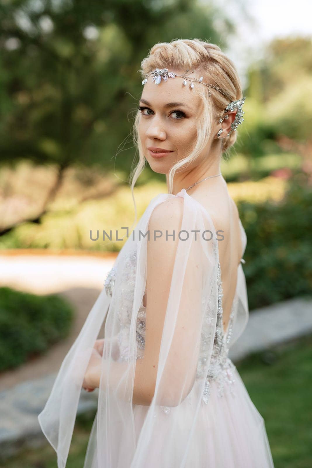 portrait of a happy bride in a light light dress on a green meadow in the park wearing elven accessories