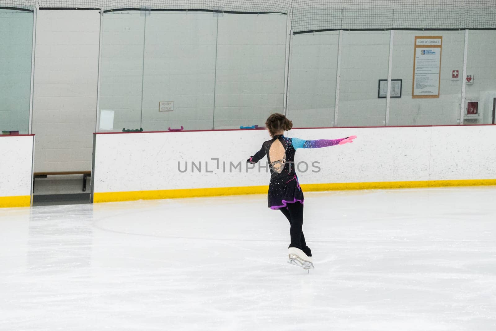 Young girl perfecting her figure skating routine while wearing her competition dress at an indoor ice rink.