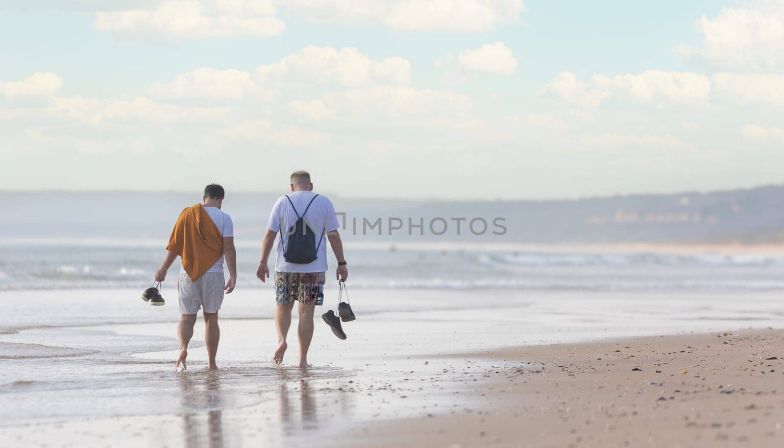A couple of men walking along a beach next to the ocean