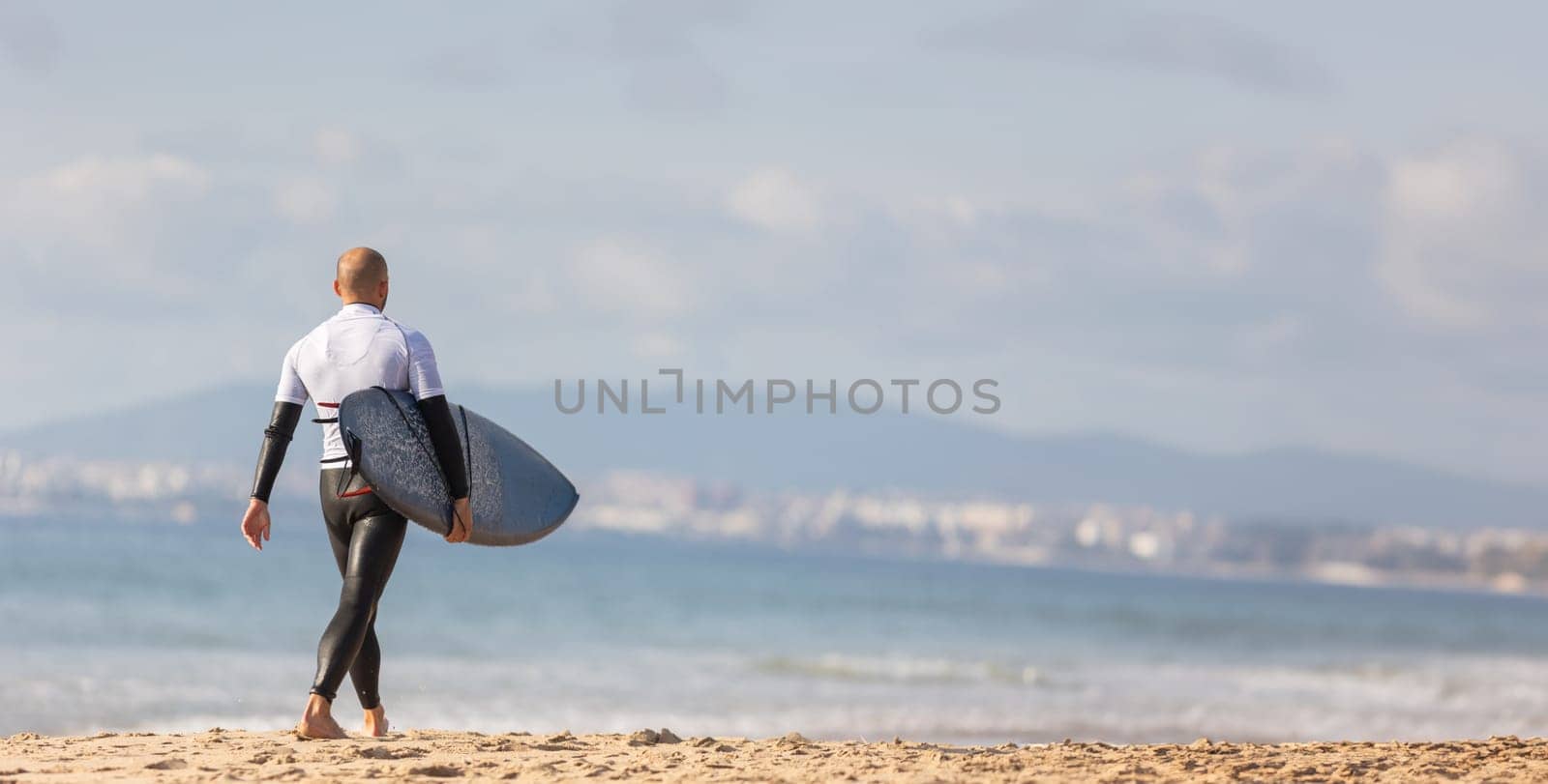 Surfing the Waves: A Man Carrying a Surfboard on a Serene, Sunlit Sandy Beach by Studia72