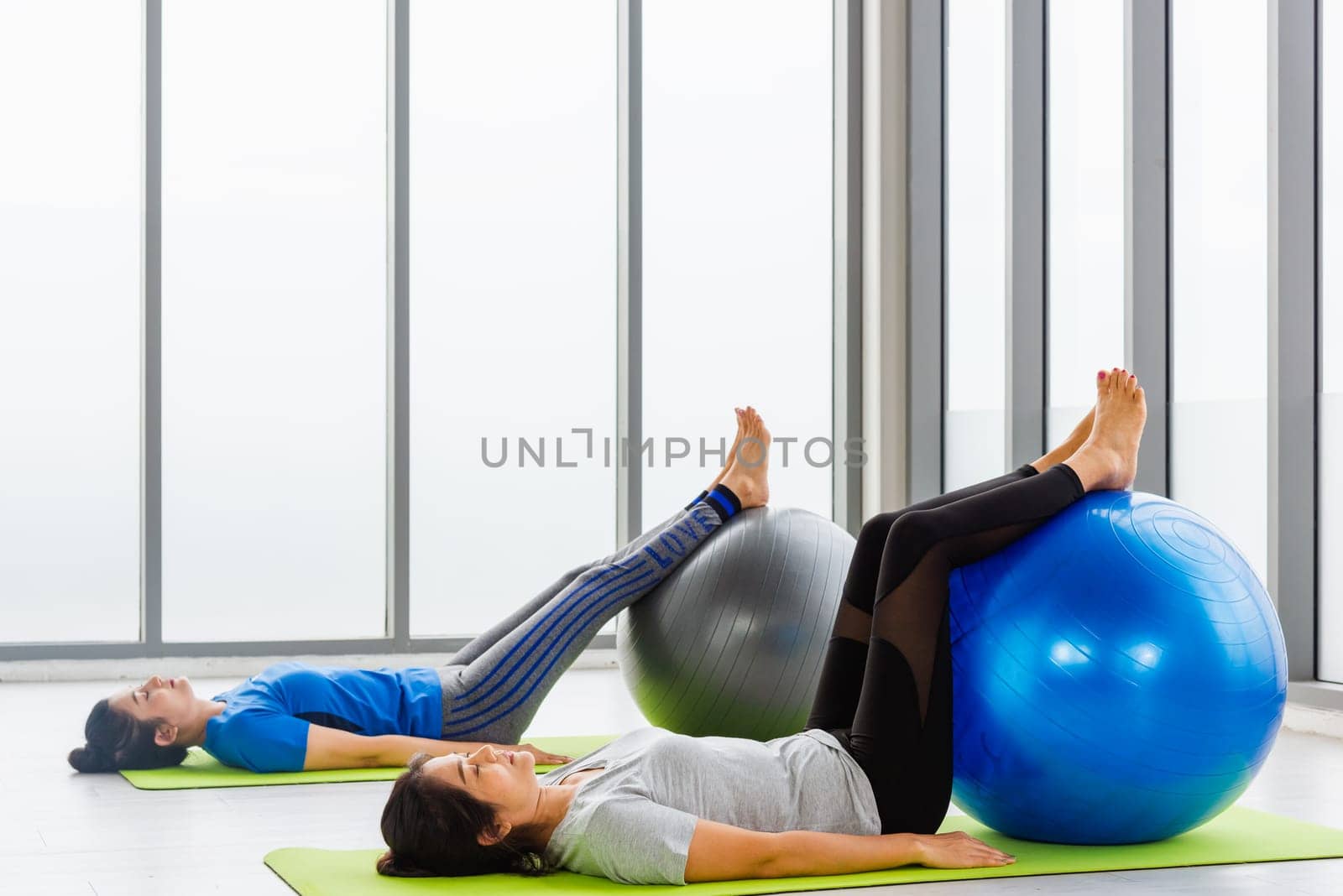 Two Asian adult and young woman in sportswear doing aerobics yoga exercise abdominal with fitness ball indoor yoga studio, fit sport healthy workout lifestyle exercise