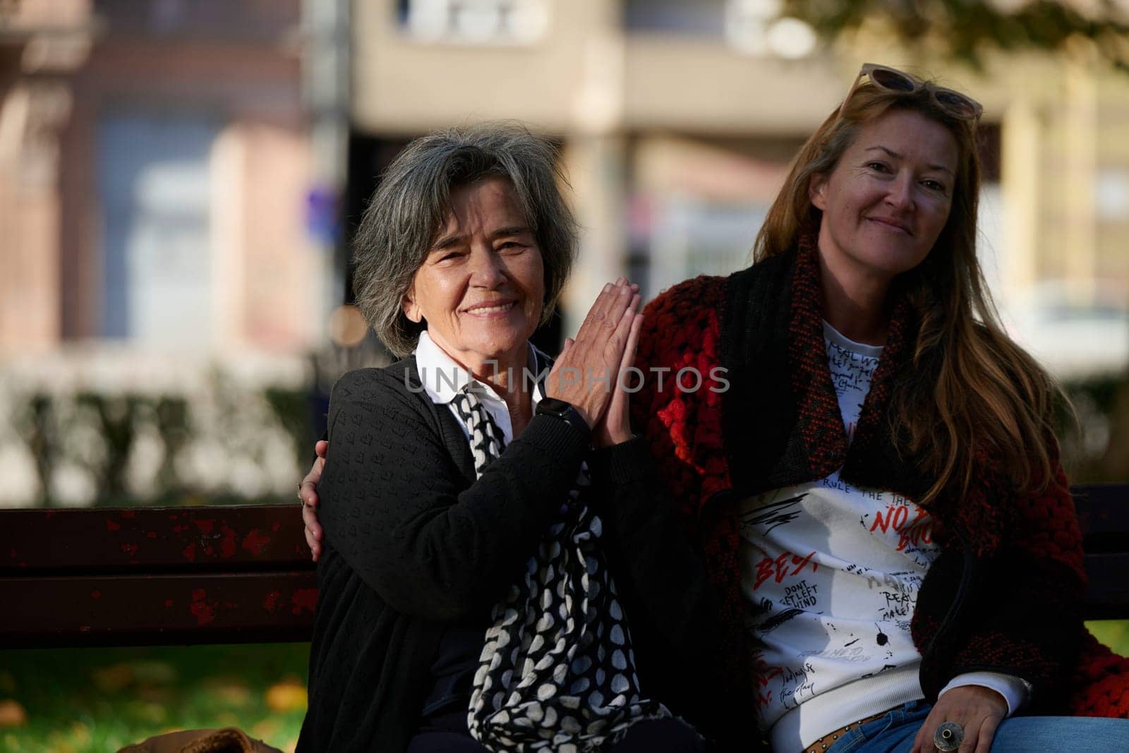 Elderly old cute woman with Alzheimer's very happy and smiling when eldest daughter hugs and takes care of her in park in autumn. Theme aging and parenting, family relationships and social care.