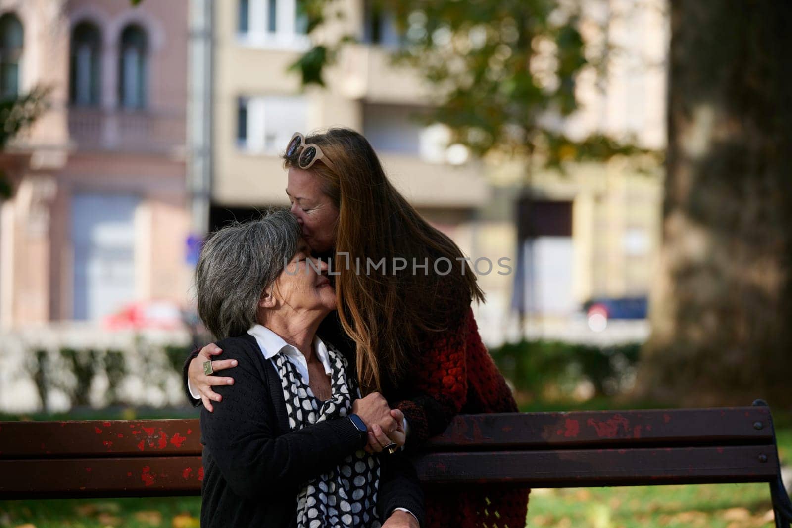 Elderly old cute woman with Alzheimer's very happy and smiling when eldest daughter hugs and takes care of her in park in autumn. Theme aging and parenting, family relationships and social care.