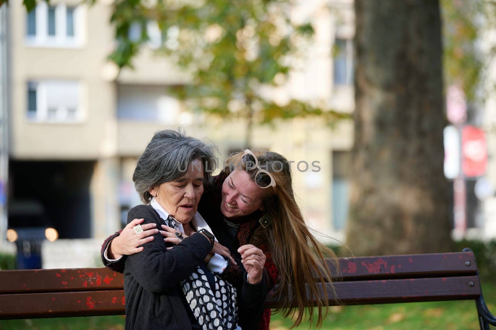 Elderly old cute woman with Alzheimer's very happy and smiling when eldest daughter hugs and takes care of her in park in autumn. Theme aging and parenting, family relationships and social care.