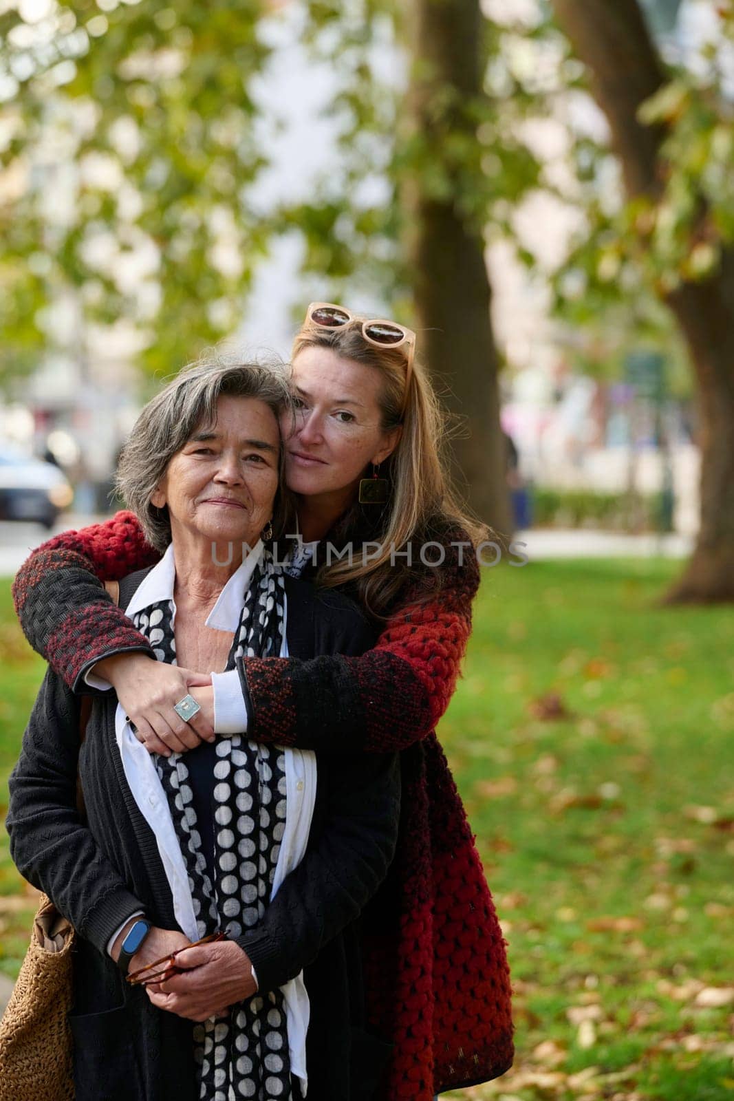 Elderly old cute woman with Alzheimer's very happy and smiling when eldest daughter hugs and takes care of her in park in autumn. Theme aging and parenting, family relationships and social care.