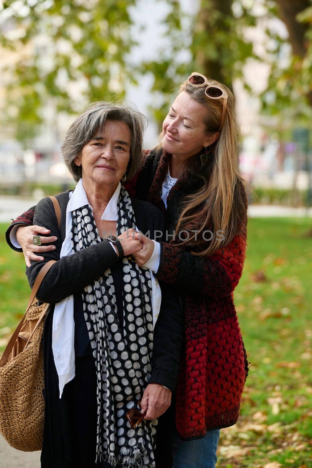 Elderly old cute woman with Alzheimer's very happy and smiling when eldest daughter hugs and takes care of her in park in autumn. Theme aging and parenting, family relationships and social care.