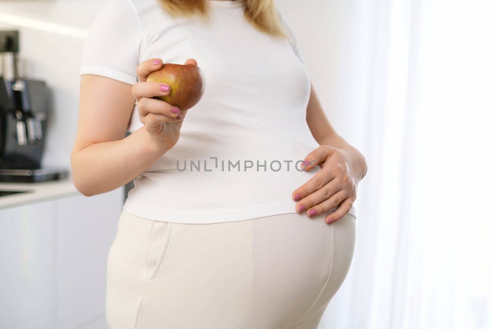 A pregnant woman is holding an apple and put her hand on her stomach. Diet during pregnancy concept.