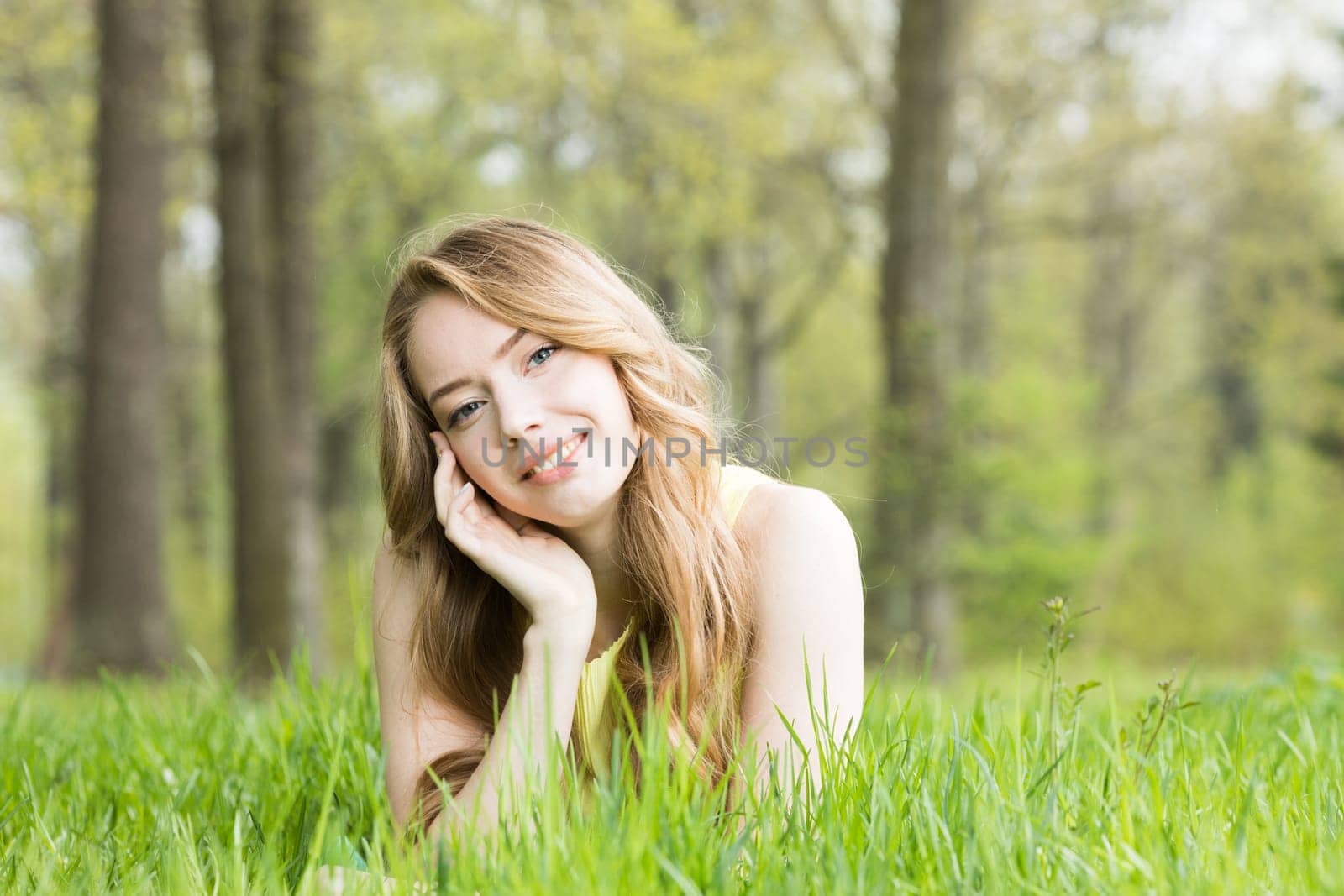 Blonde pretty girl laying on the grass in spring park and smiling