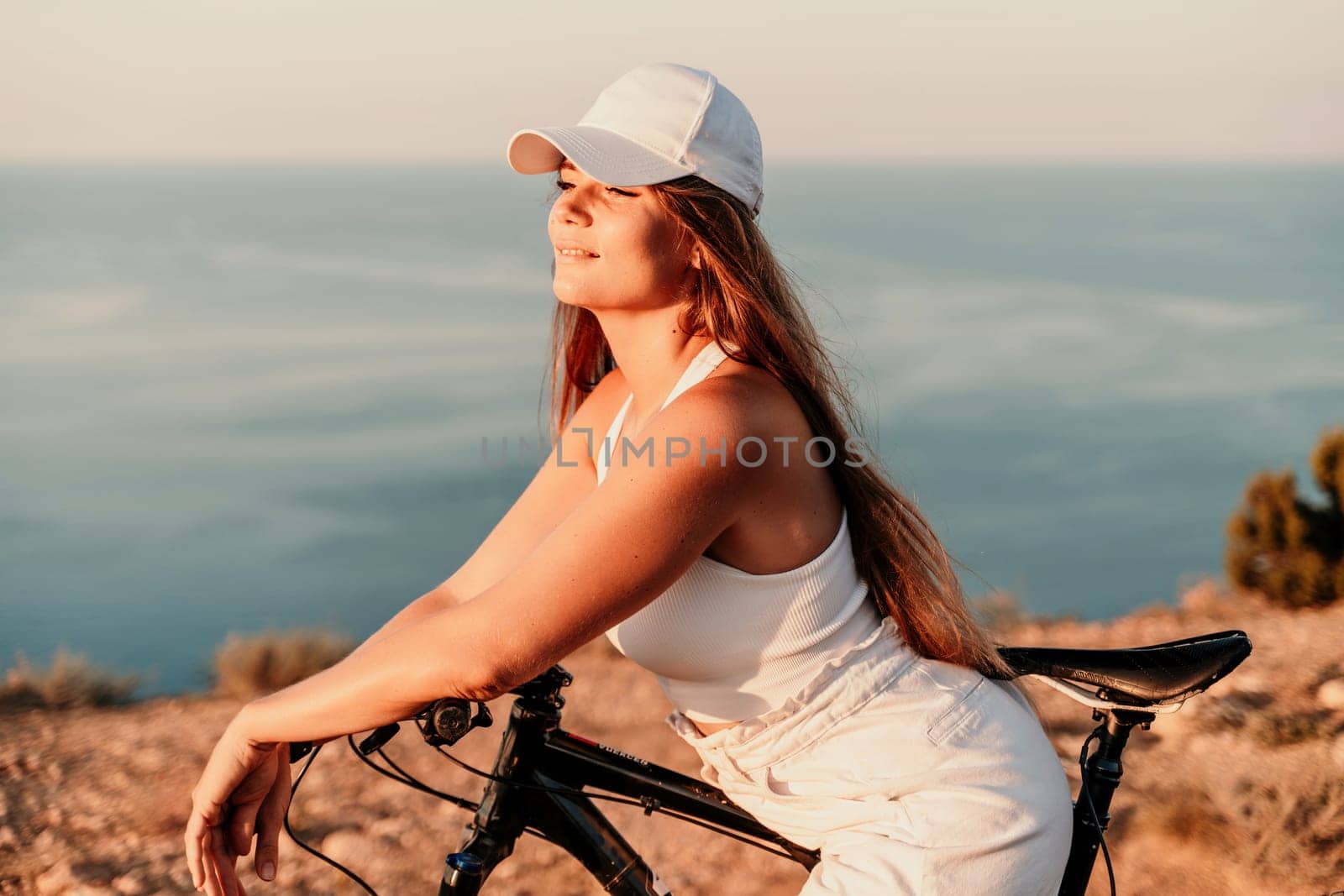 A woman cyclist on a mountain bike looking at the landscape sea. Adventure travel on bike. by Matiunina