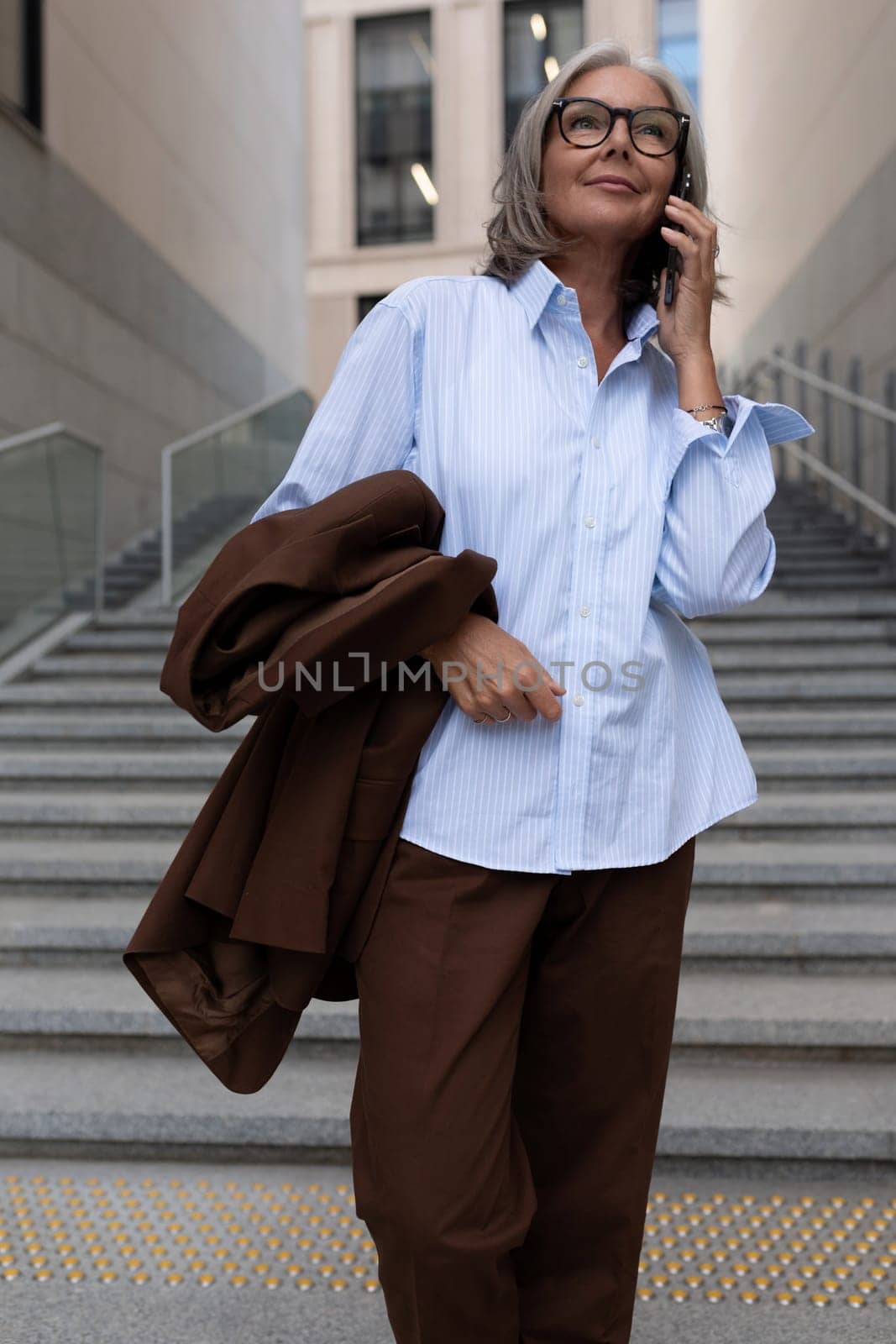 60 year old pretty caucasian business lady dressed in an elegant manner discusses project tasks using a smartphone.