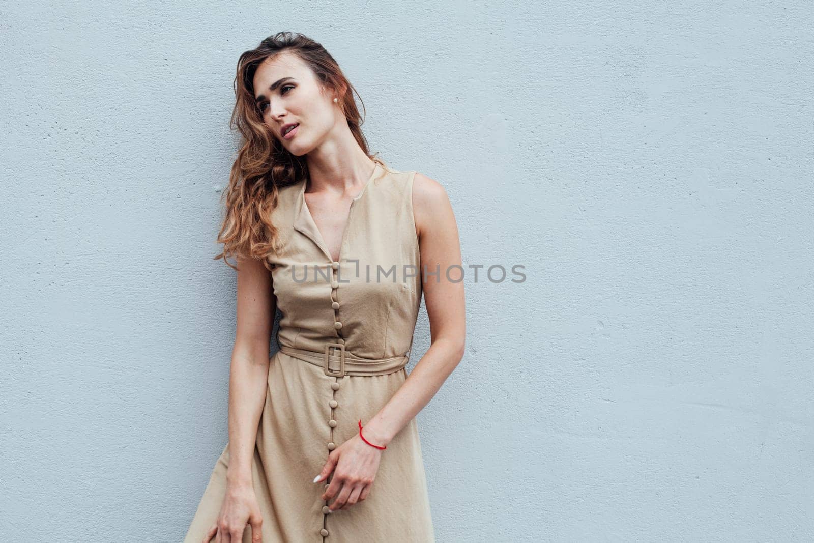 Portrait of a beautiful fashionable woman in a beige dress against a grey background