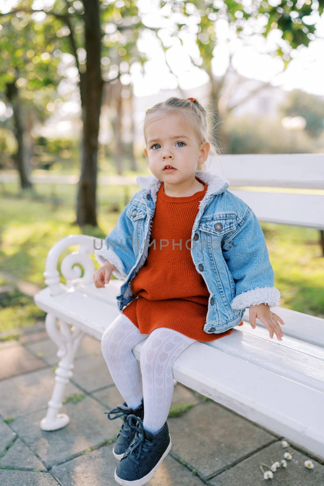 Little girl sits thoughtfully on a white bench in the park. High quality photo