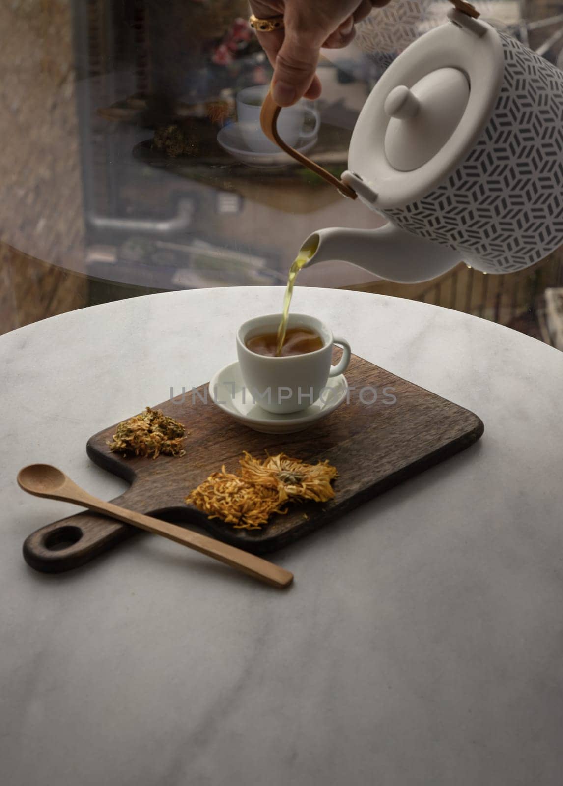 Pouring Chinese chrysanthemum flower tea from Ceramic teapot into a white teacup on wooden cutting board. Dried chrysanthemum flower, Healthy beverage for drink, Space for text, Selective focus.