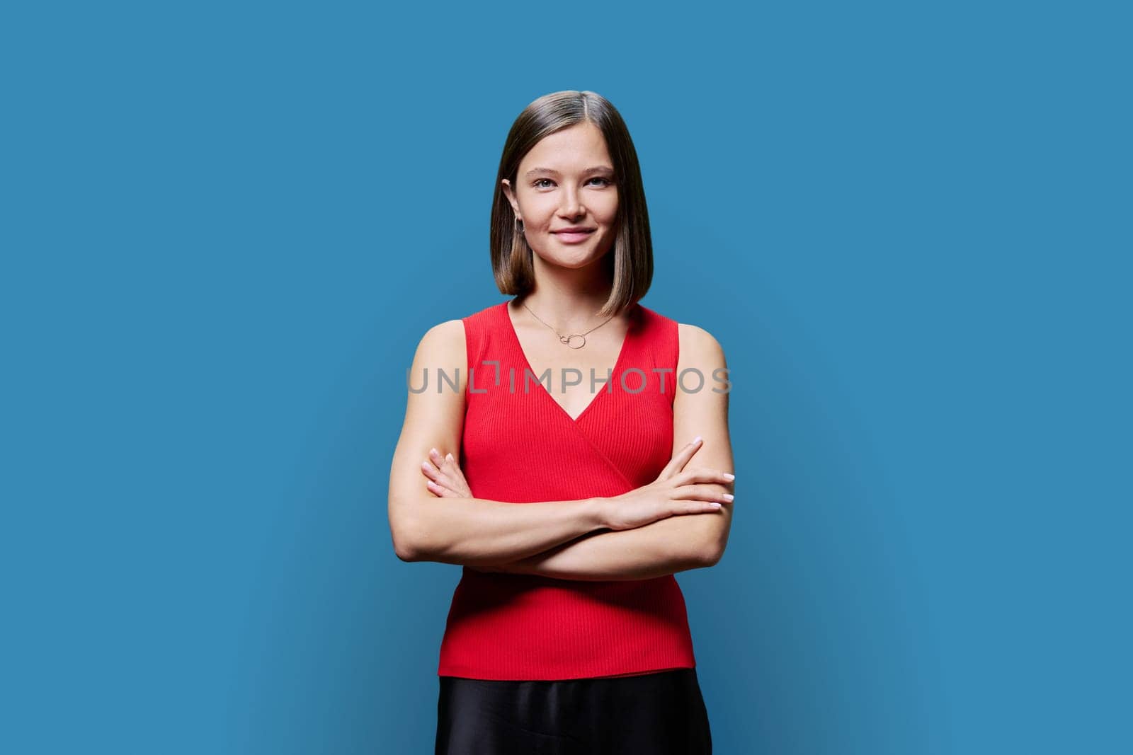 Portrait of young confident woman in red on blue studio background by VH-studio