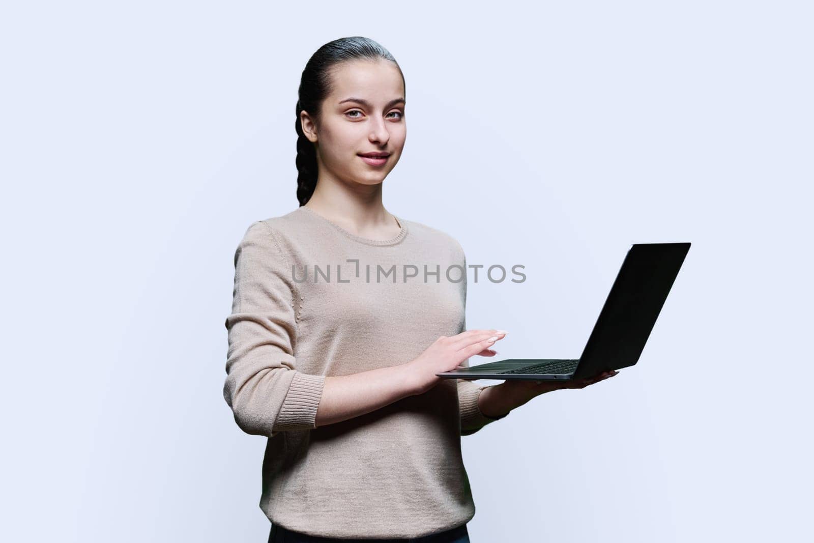 Teen girl high school student using laptop looking at camera on white studio background. Technology, e-learning, education, adolescence, youth concept.