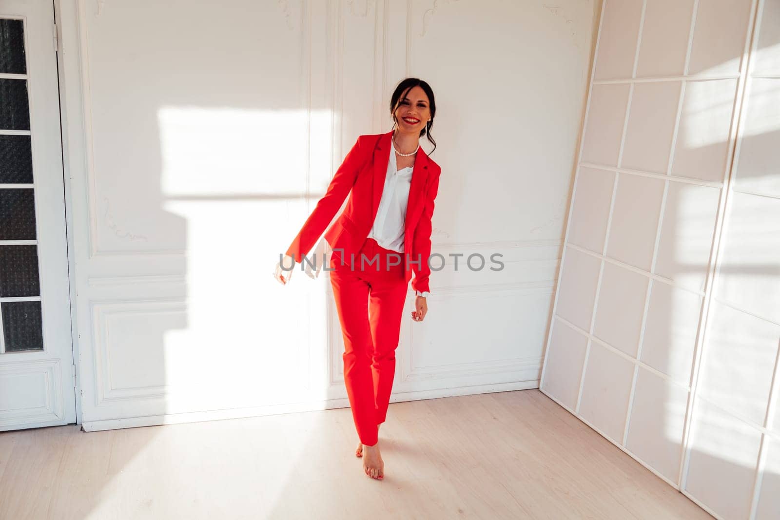 Portrait of a brunette woman in a red business suit in a white room by Simakov
