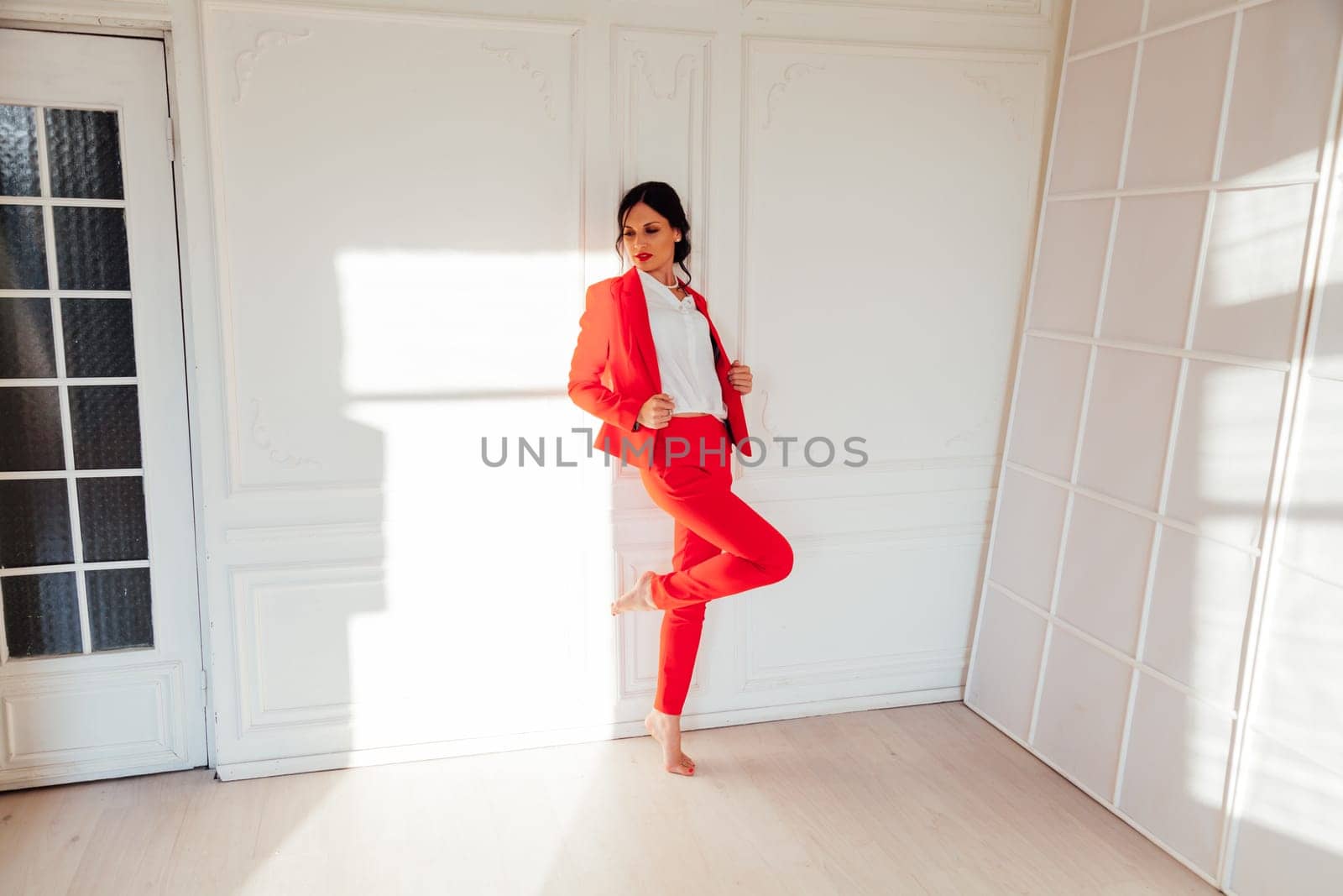 Portrait of a brunette woman in a red business suit in a white room