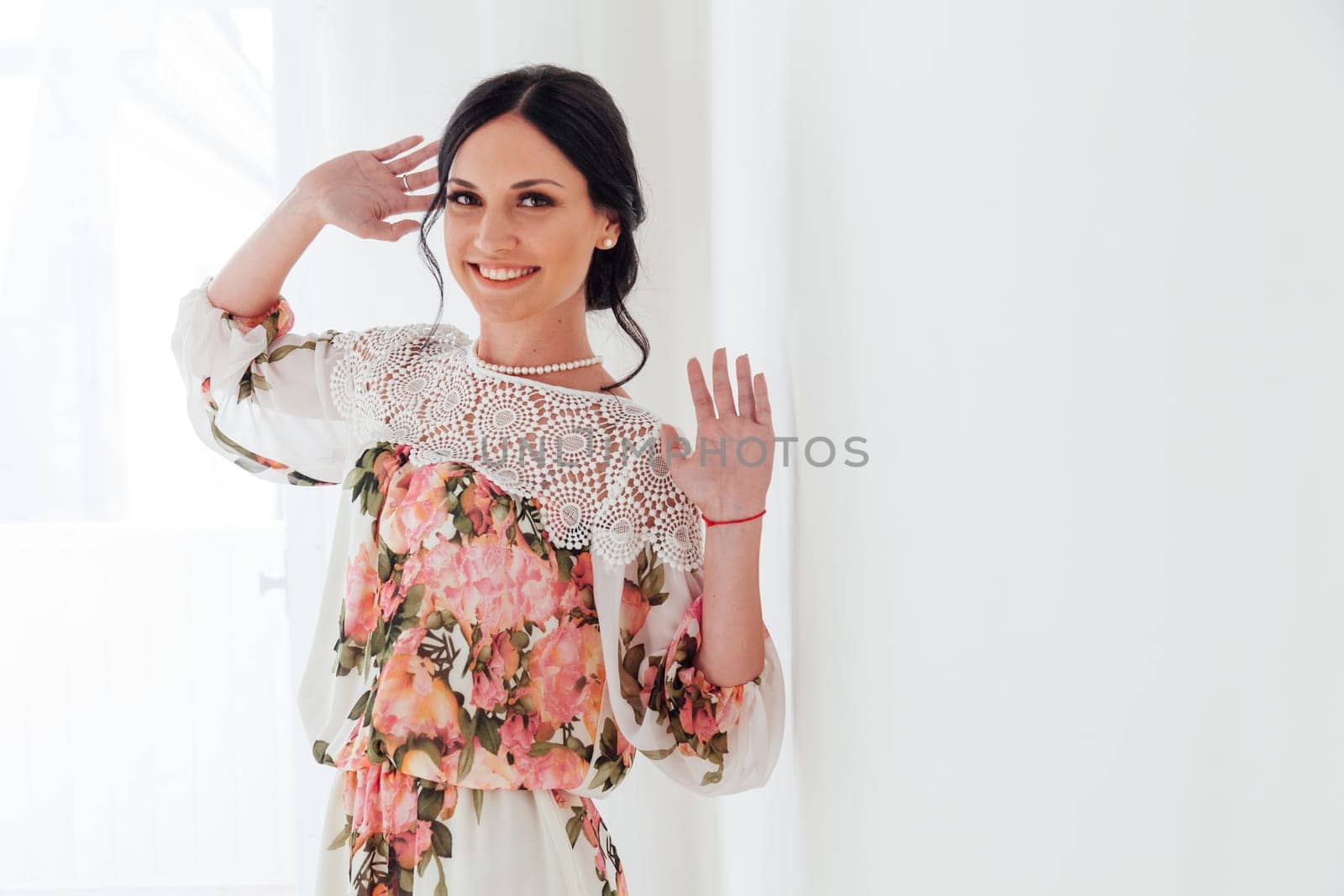 Portrait of a brunette woman in a dress with flowers in a white room by Simakov
