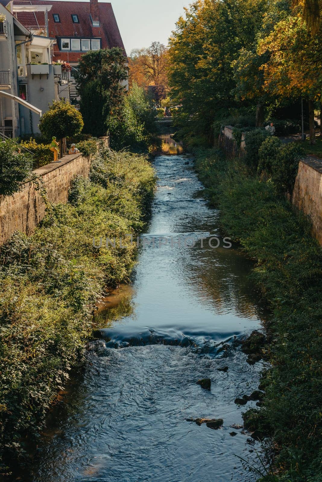 Beautiful small river with clean and clear water front of colorful autumn trees and small old town on the hill agaist nice blue and clouds sky during autumn in Europe.