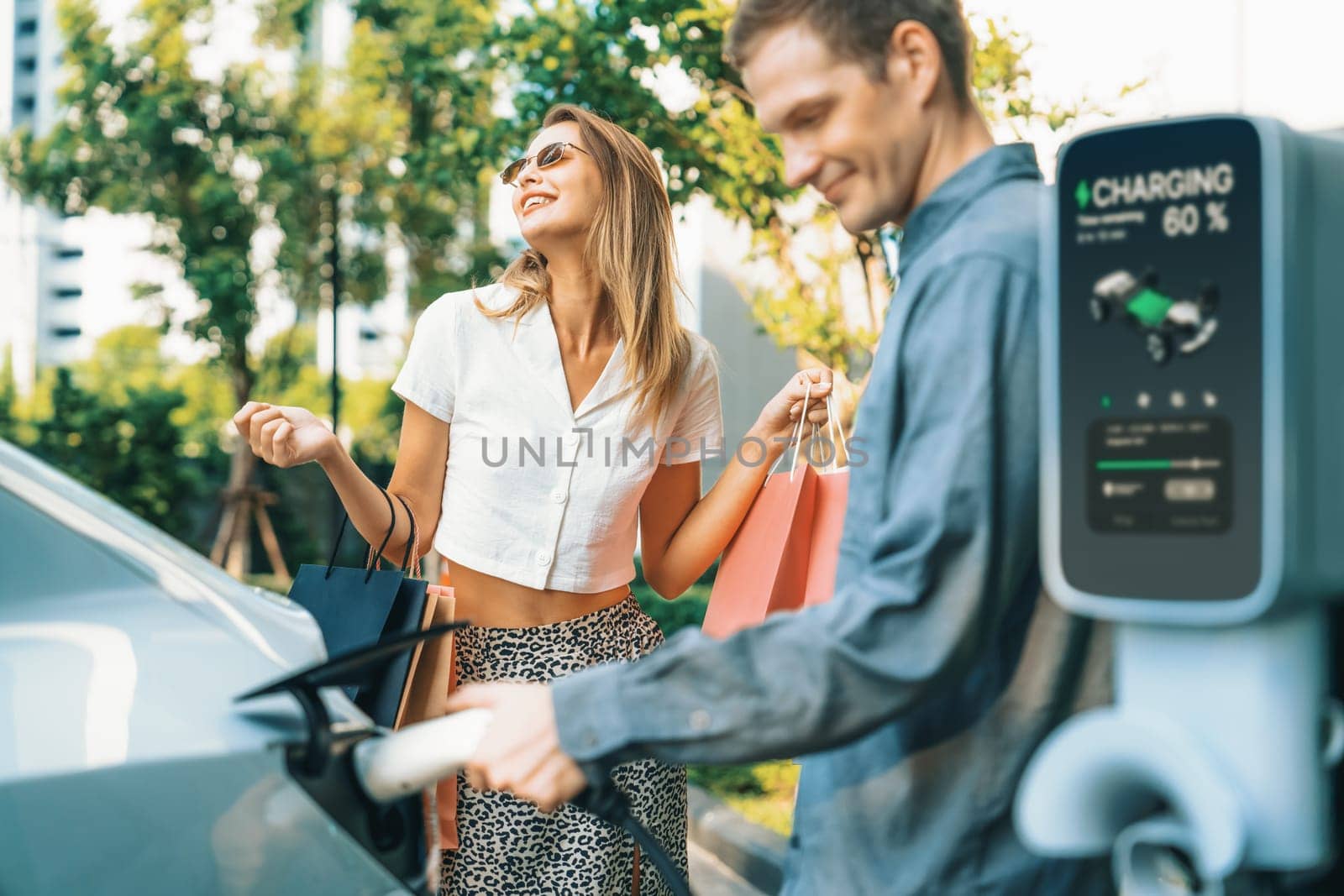 Young couple travel with EV electric car in green sustainable city innards by biancoblue