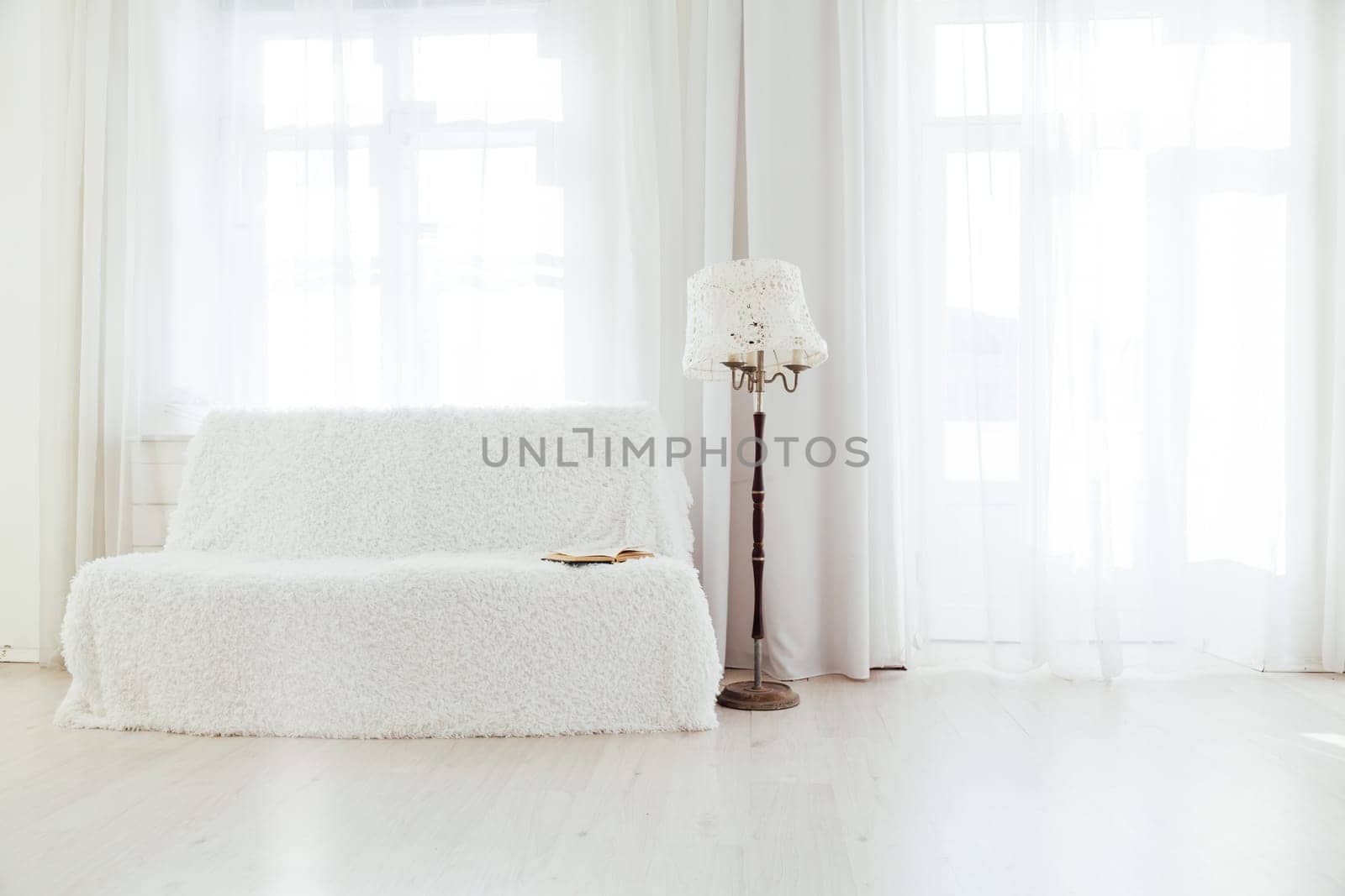 white sofa with a book in the interior of a white room with windows by Simakov