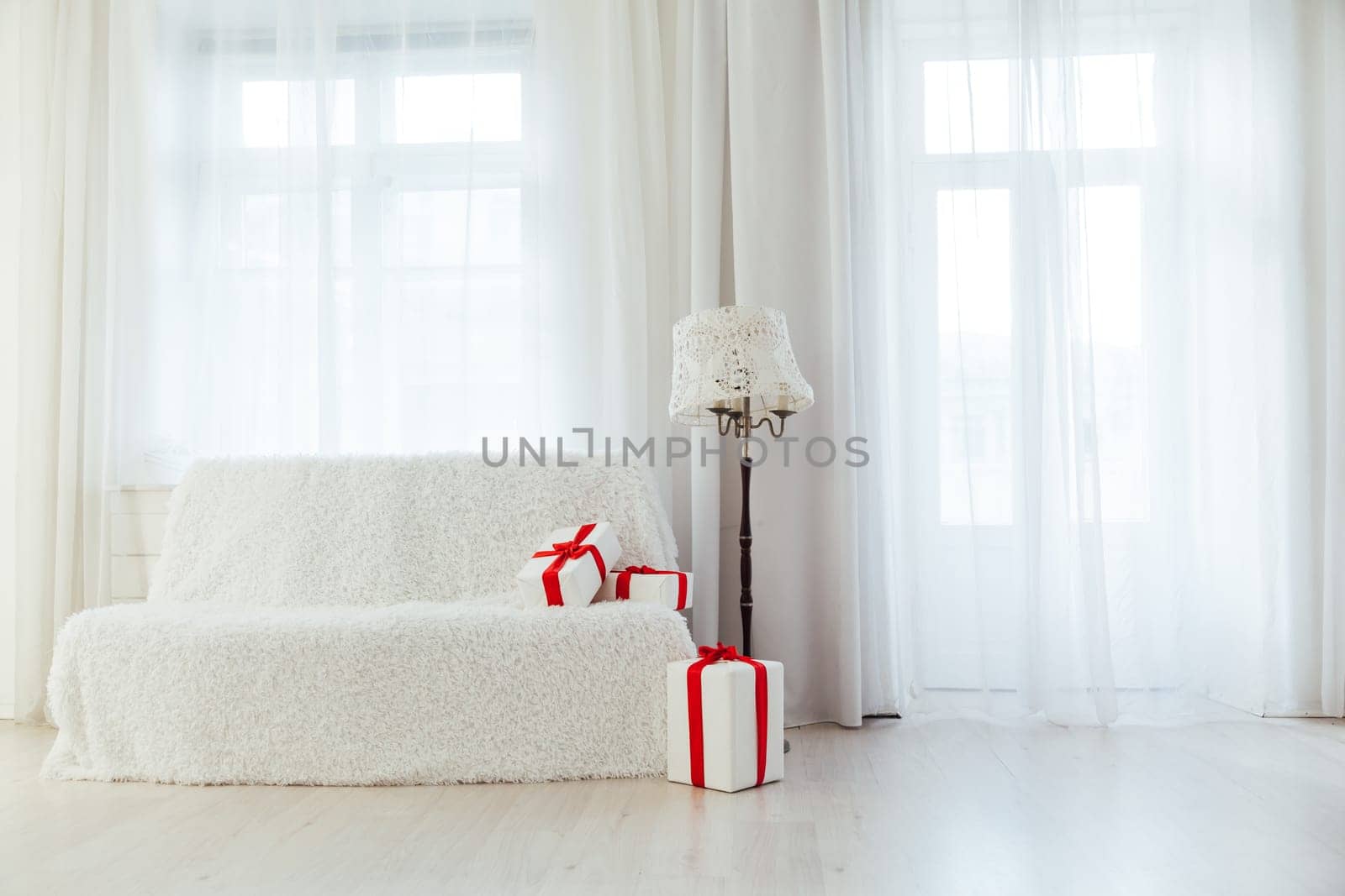 white sofa with gifts in the interior of the white room with windows by Simakov